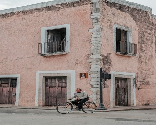 A person commuting to work on a bicycle passing by a mural in a Mexican city